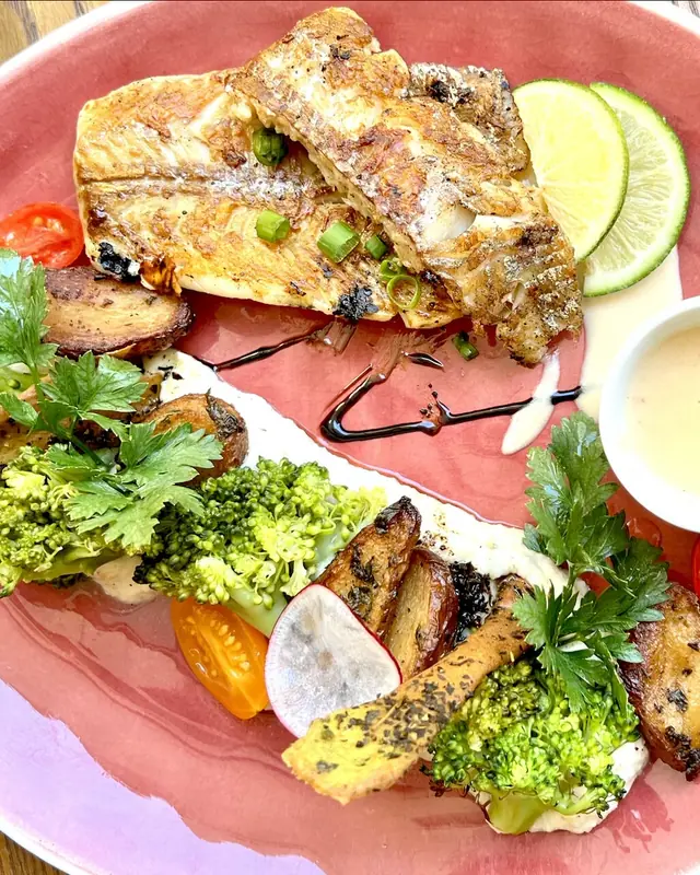 Filet de poisson grillé, légumes rôtis, brocoli et citron vert sur une assiette rose