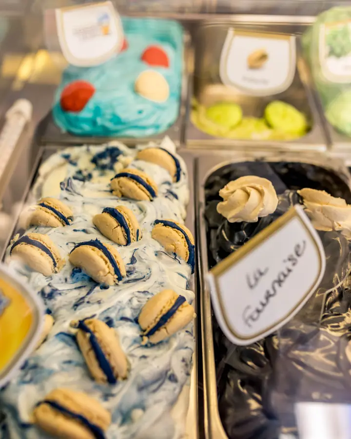 La vitrine des glaces : un bac marbré de bleu garni de macarons, et un bac de glace noire coiffée de meringues, étiqueté La Fournaise
